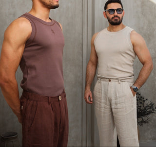 Two men wearing everseason tank tops and pants standing against a gray wall.
