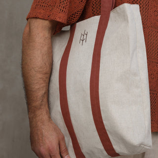 Man wearing beige and brick Everseason linen tote bag against a gray wall.