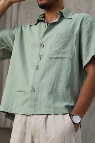 Person wearing a light green short-sleeve shirt with a pocket, standing against a neutral background.