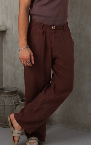 Man wearing a brown Everseason 100% linen pants leaning against a gray wall.