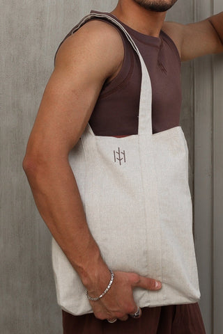 Man wearing sunglasses and a sleeveless shirt with a linen Everseason tote bag against a gray wall